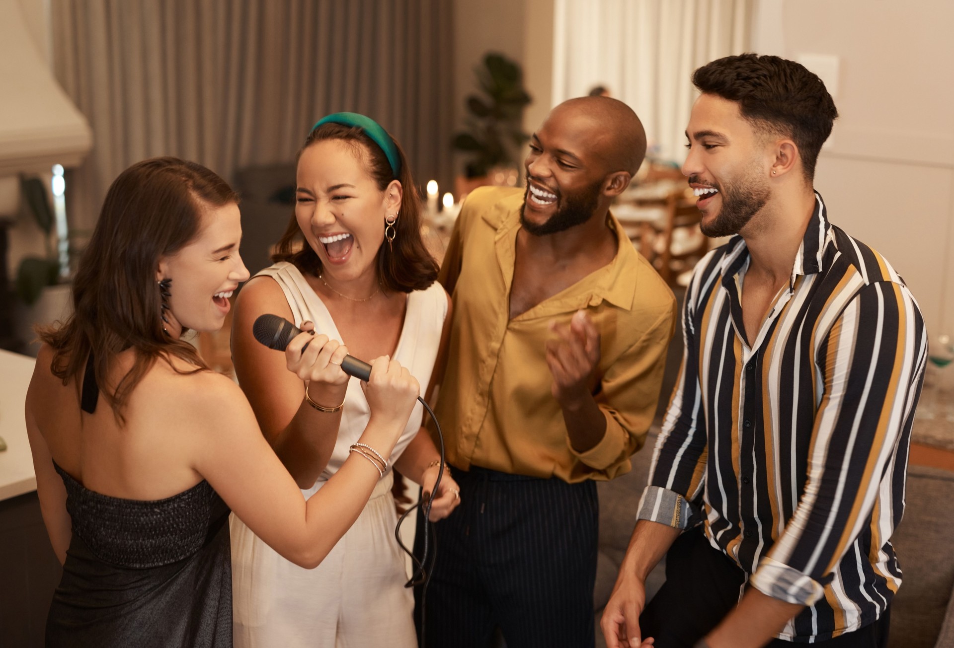 Shot of a diverse group of friends standing together and singing karaoke at a dinner party